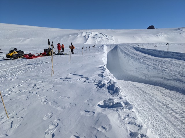 A group of people standing at the edge of an exevated ditch used to simulate a crevasse