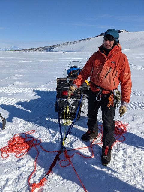 Mike stands next to the back of a snowmobile with a rescue anchor attached to it