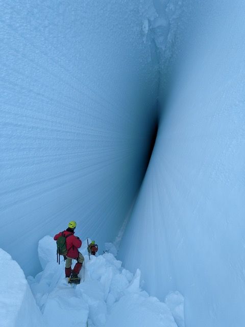 2 people stand on the bottom of a ramp going down into a deep ice crevasse