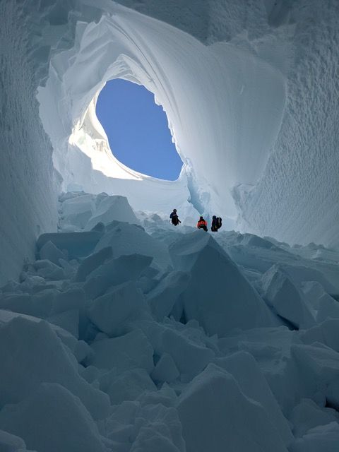 3 people stand beneath a sky light in the ice cave