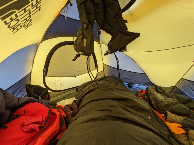 View of the inside of a mountain tent. A sleeping bag is in the center with bags and clothing surrounding