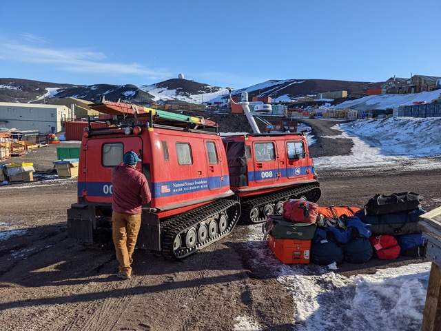 Bags piled next to a 2 cab Hagglung tracked vehicle on a dirt road in McMurdo