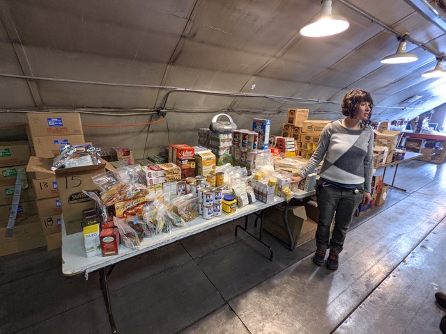 A person stands next to 3 tables full of packaged food