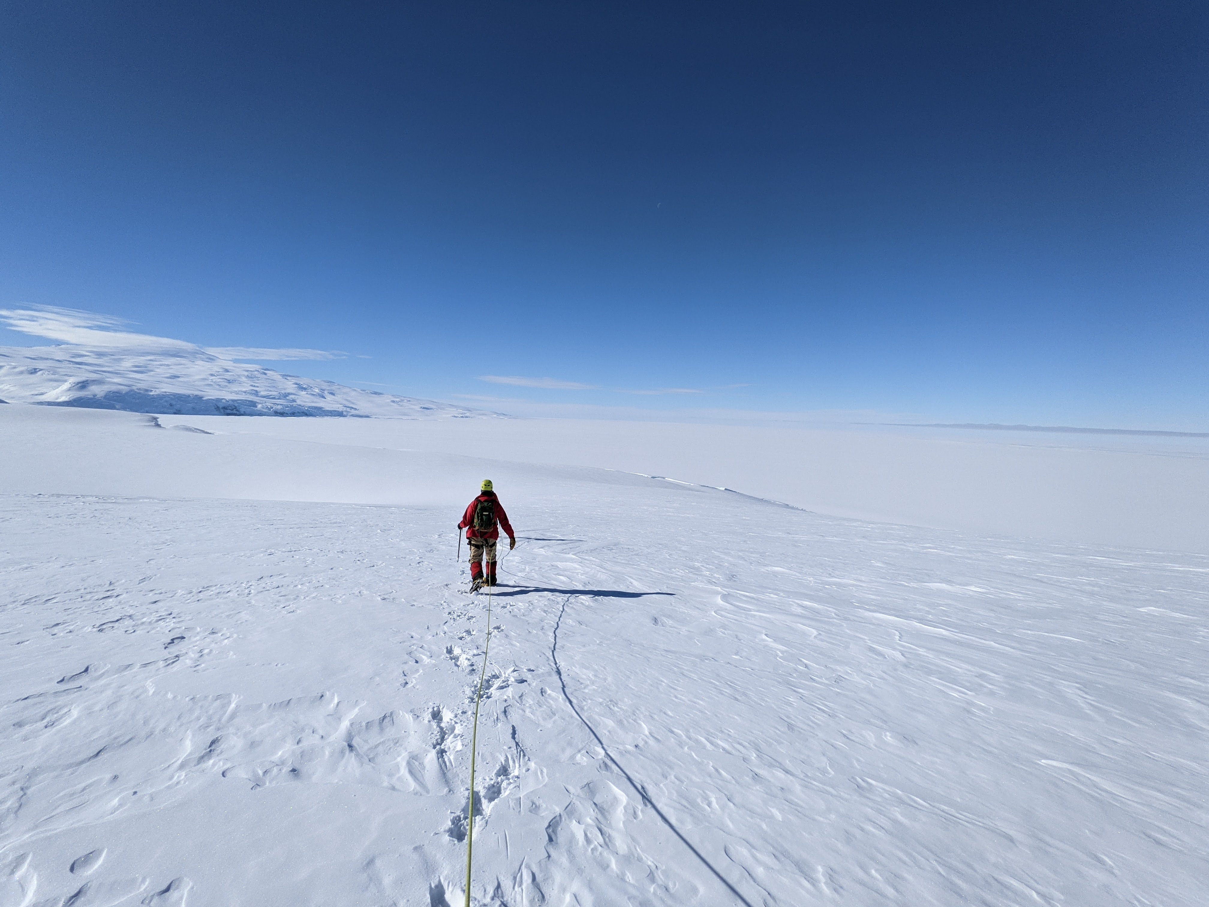 A person walks downslope in the snow overlooking a flat ice shelf