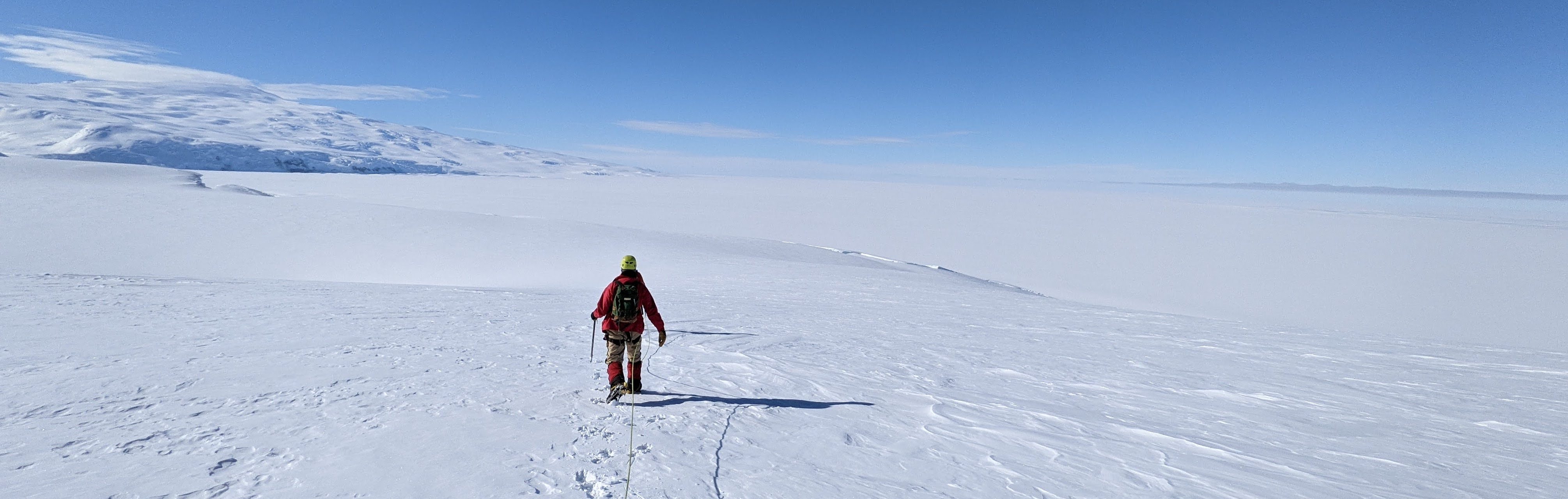 A person walks downslope in the snow overlooking a flat ice shelf