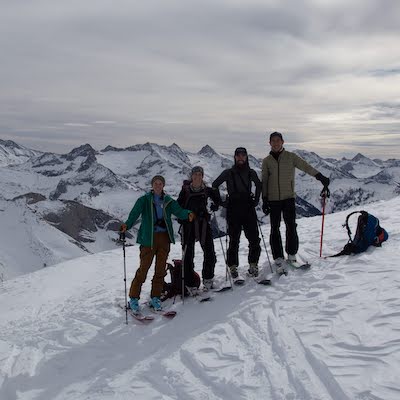  4 people on skis pose for a picture on a mountain ridgeline