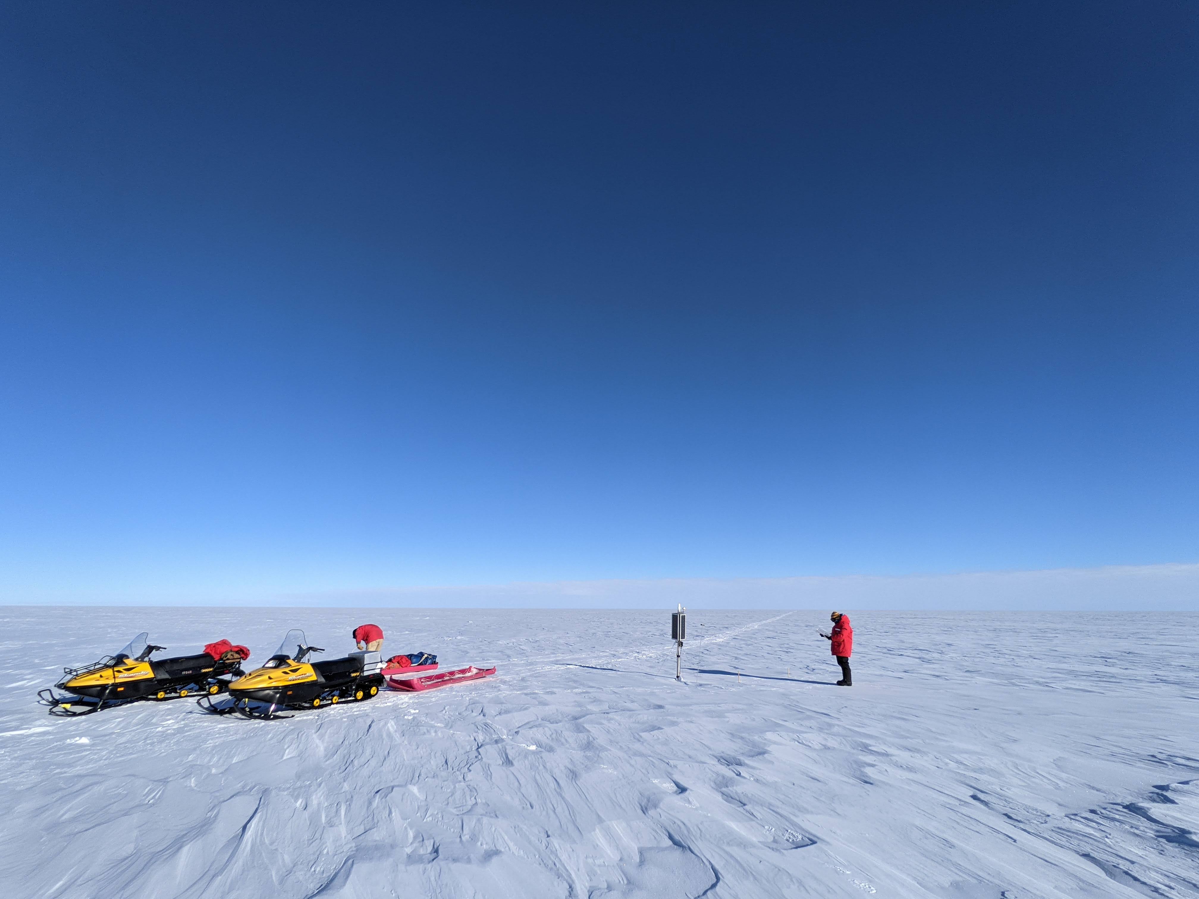 A person and 2 snowmobiles on an ice sheet